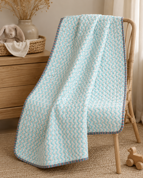 A light aqua and white chevron-patterned quilted blanket draped over a wooden chair in a cozy nursery setting.