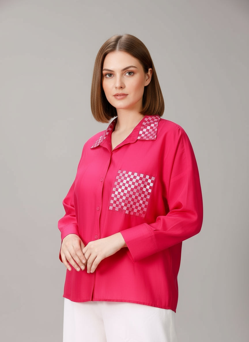 A model wearing a fuchsia pink cotton silk oversized shirt with mirror embroidery, paired with white trousers.
