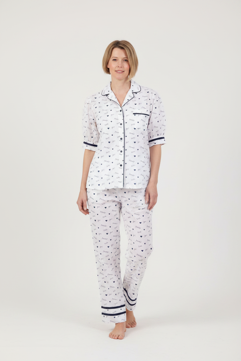A woman modeling a two-piece pajama set featuring a white base with a small navy blue pattern, a short-sleeve button-up top, and matching long pants, set against a plain light gray studio background.