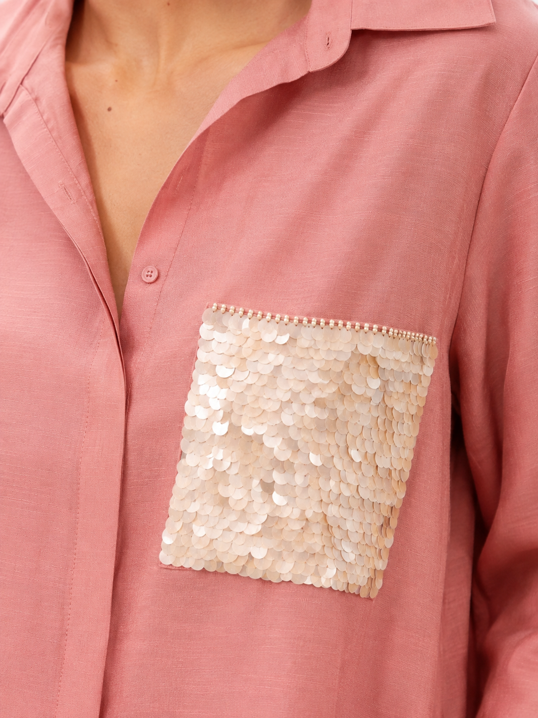 A close-up of a dusty pink button-up shirt featuring a large, square sequined chest pocket in a champagne beige tone.
